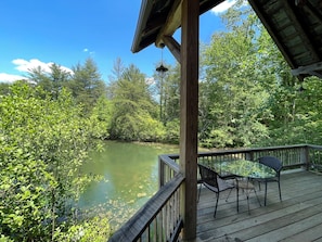 Eine Holzterrasse mit einem Glastisch und Stühlen mit Blick auf ein von Bäumen umgebenes Gewässer.