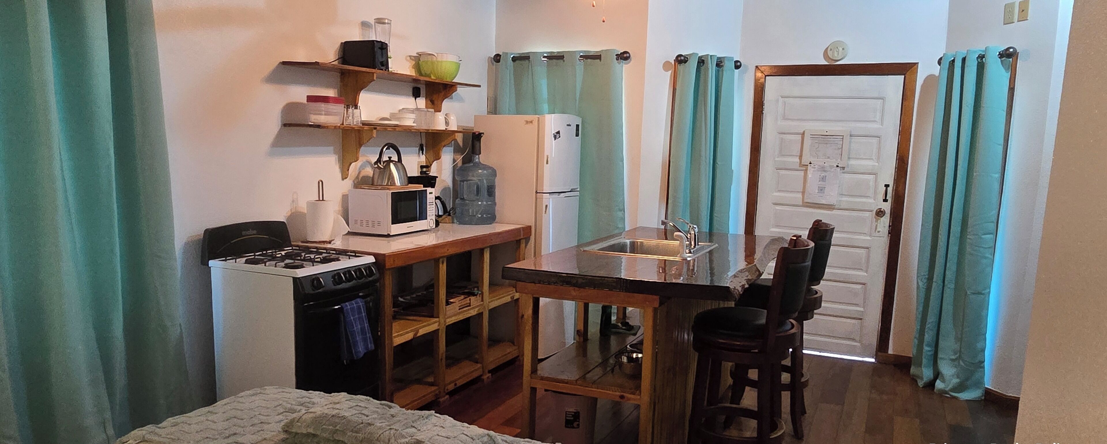A compact kitchen with a stove, microwave, refrigerator, and a small bar area.