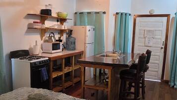 A compact kitchen with a stove, microwave, refrigerator, and a small bar area.