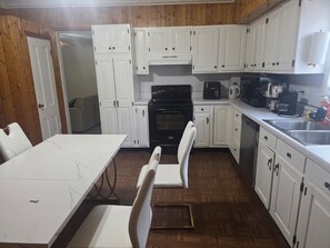 A kitchen with white cabinets, a dining table, chairs, a stove, a microwave, and a coffee maker.