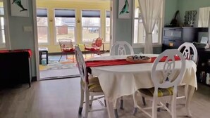 A dining area with a table set for four, chairs, a fan, and a window with curtains. - Mermaid's Mini Mansion (Eastport)