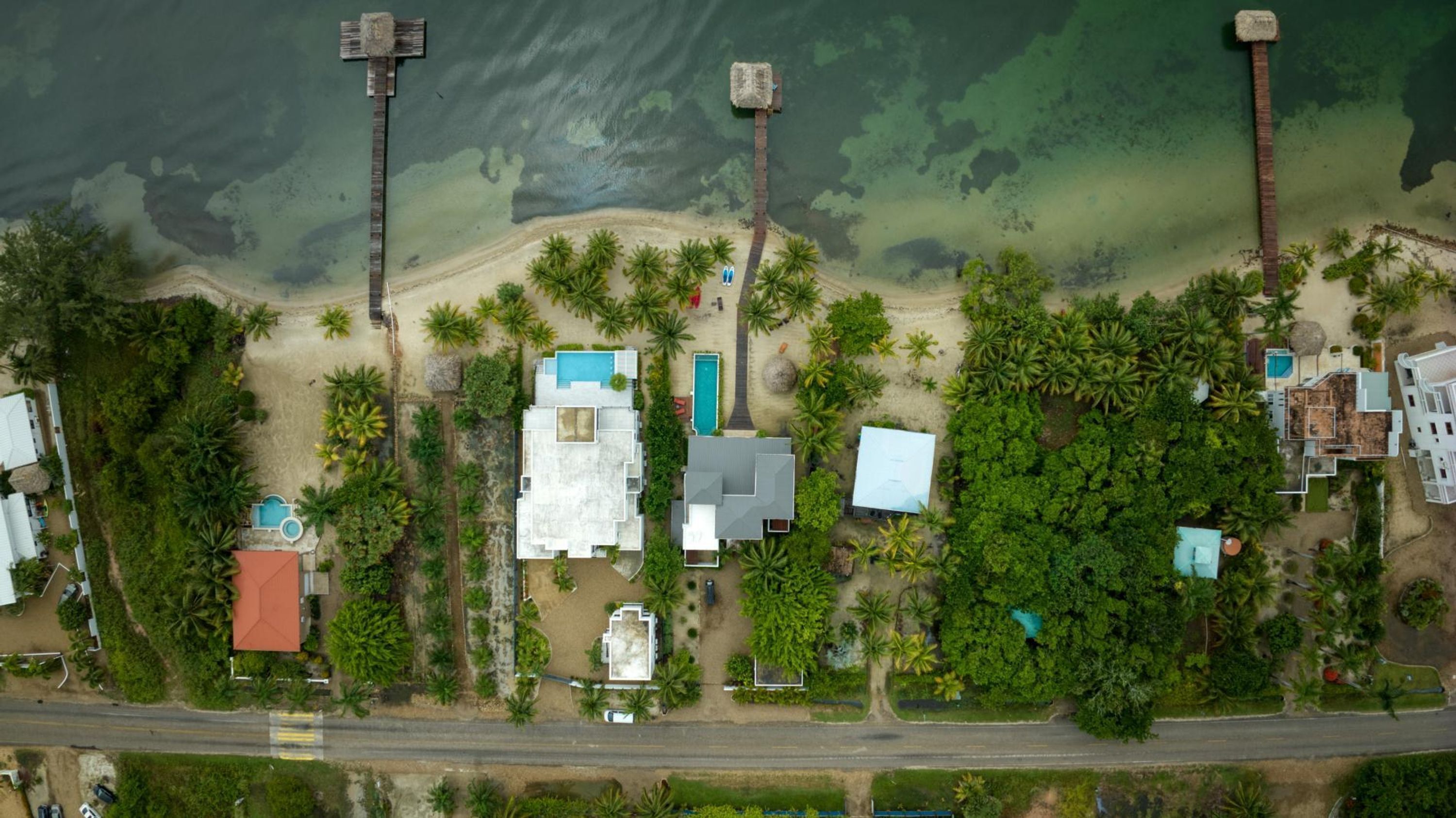 Vue aérienne d’une propriété située sur la côte, comprenant plusieurs bâtiments, une plage et des palmiers.