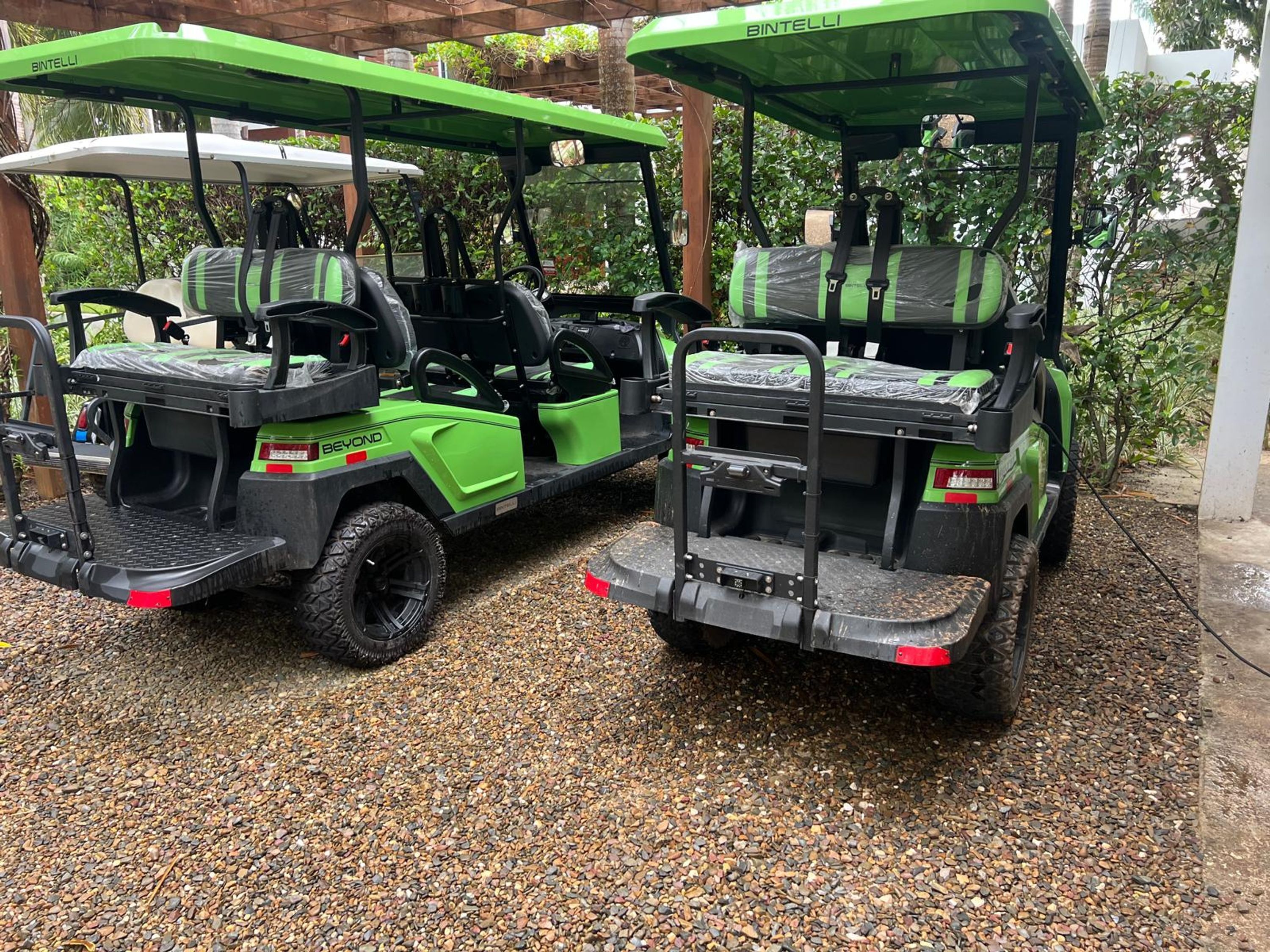 Two golf carts with green and black colors, labeled 'BINTELLI' and 'BEYOND,' parked on a gravel surface.