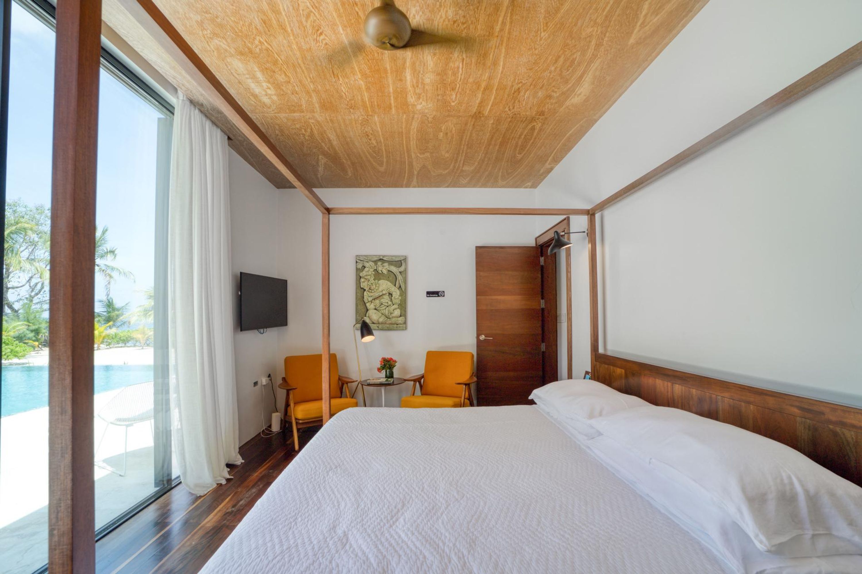 Hotelkamer met een groot bed, twee stoelen, een televisie en een deur naar een balkon met uitzicht op een zwembad.