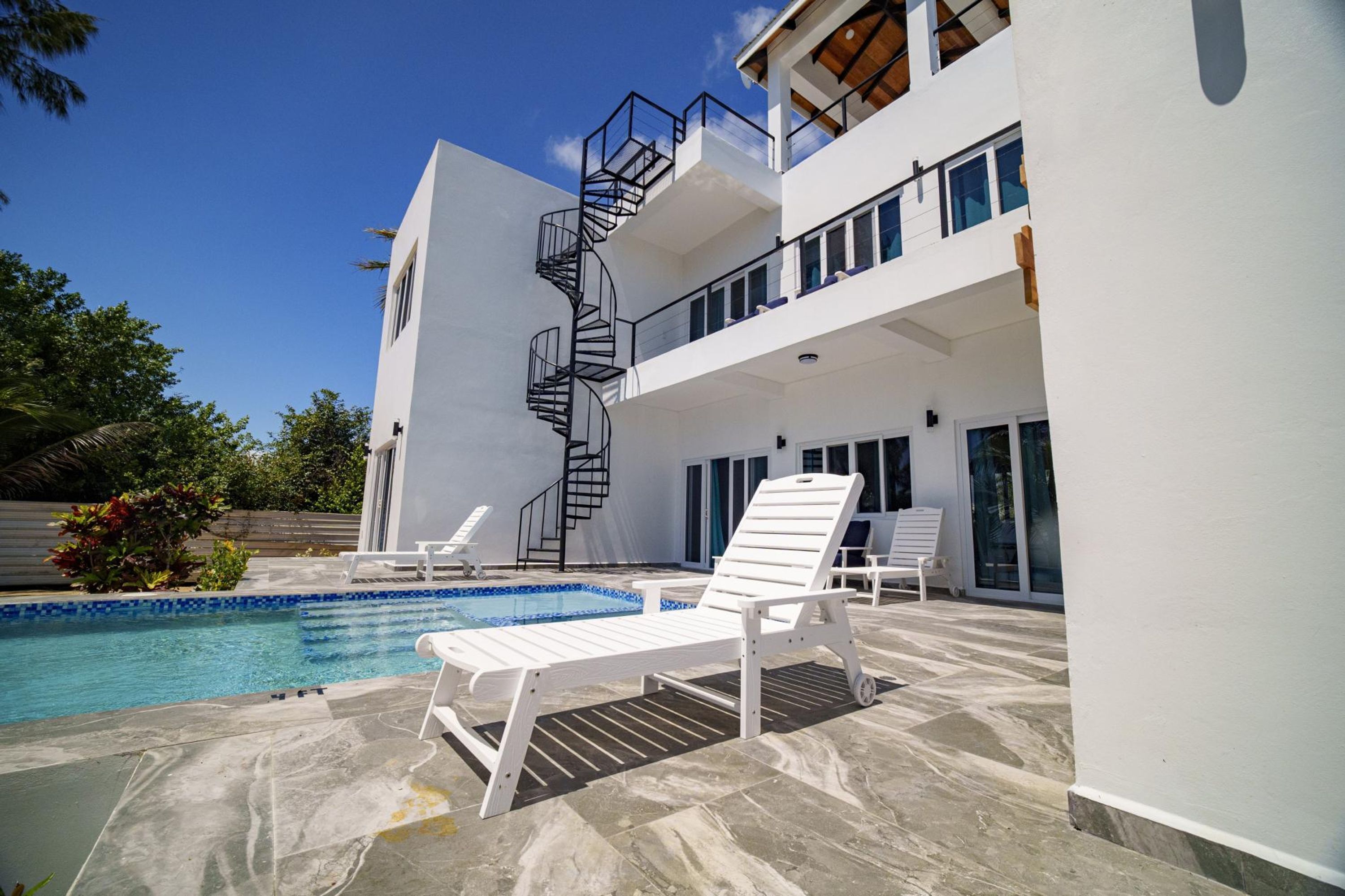 A modern two-story building with a spiral staircase, a swimming pool, and outdoor seating.