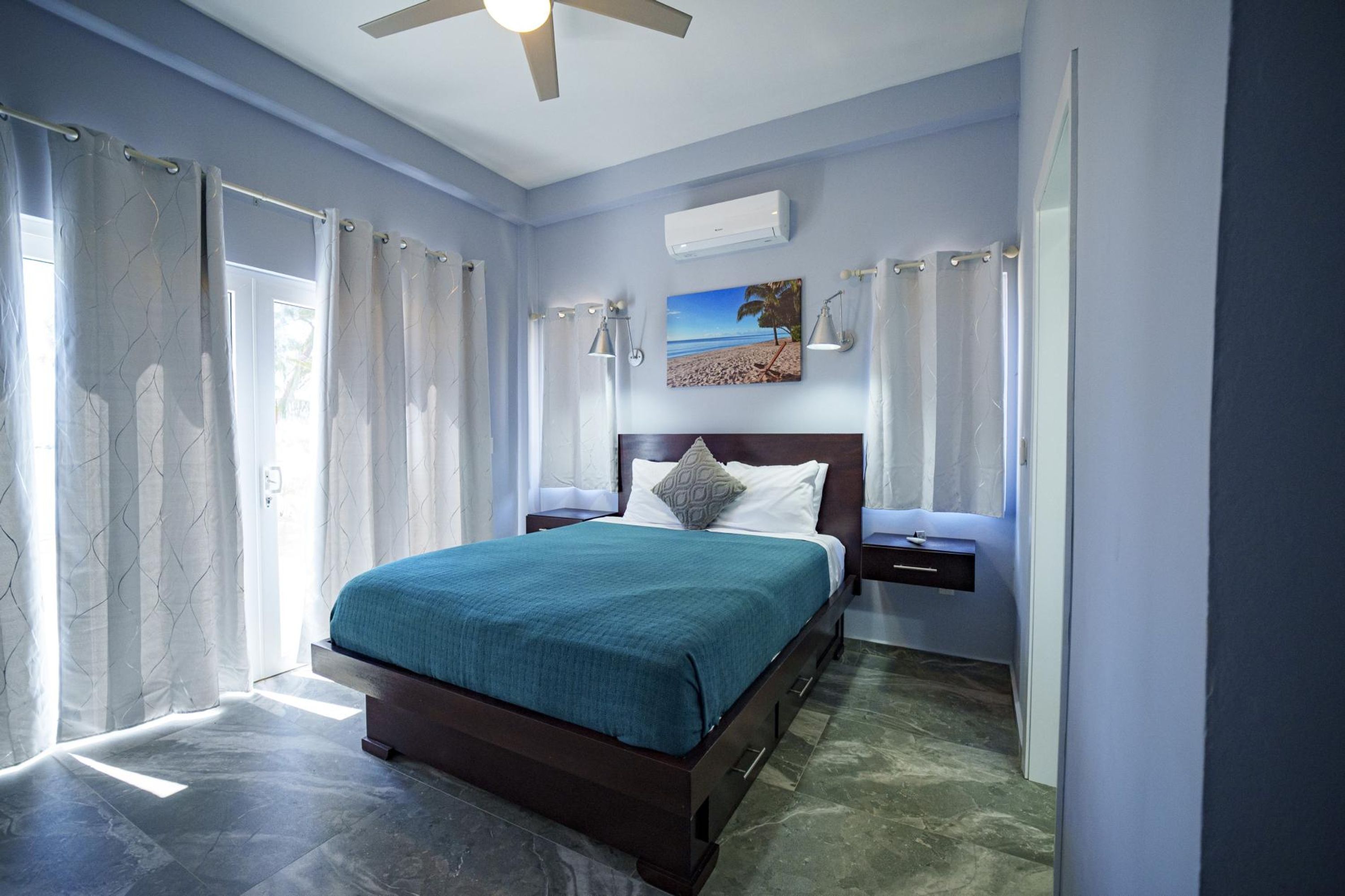 A bedroom with a bed, nightstands, an air conditioner, and a painting on the wall.