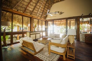 A room with a thatched roof, wooden furniture, a bed, a sofa, and a dining area with a table and chairs.