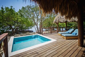 A wooden deck with a pool, lounge chairs, and a thatched roof structure.