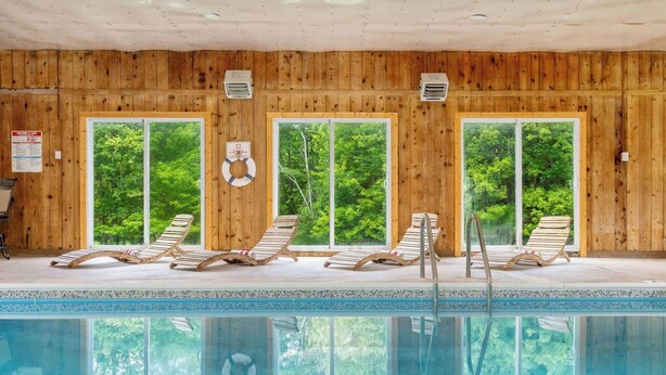 En inomhuspool med träpanel, fyra solstolar och stora fönster.