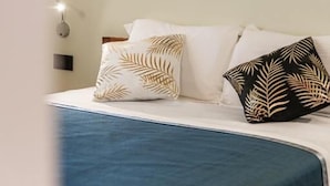A bed with a blue bedspread, white pillows, and a tropical leaf-patterned pillow. - Luxury Vatican Rooms (Rome)