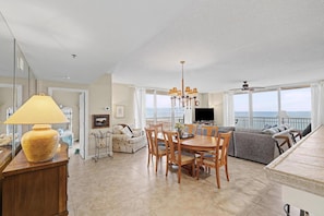 A spacious living area with a dining table, sofas, a TV, and a balcony with a view. - Emerald Coast Escape – End Unit Steps from the Sand (Pensacola Beach)