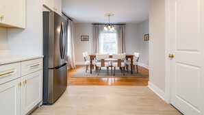 Une cuisine avec des meubles blancs, un réfrigérateur en acier inoxydable et un coin repas comprenant une table et des chaises.