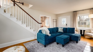 Un salon avec un canapé d’angle bleu, un escalier et une vue sur l’extérieur.