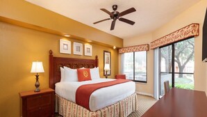 Une chambre d’hôtel équipée d’un lit, d’un bureau, d’un ventilateur de plafond et de grandes fenêtres.