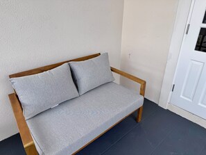 A wooden-framed sofa with grey cushions against a textured wall, positioned near a white door. - La Porta Della Casa - 2-bedroom Apartment with Pool & Sun Deck (Fitts Village)
