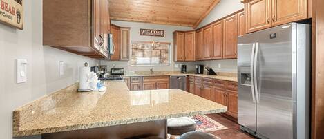 A kitchen with wooden cabinets, a stainless steel refrigerator, granite countertops, and bar stools.
