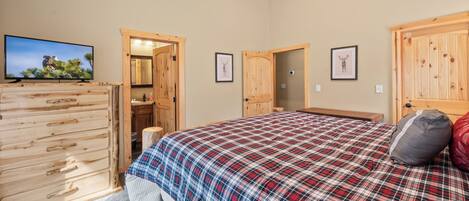 A bedroom with a plaid bedspread, wooden wardrobe, and a television on a stand.