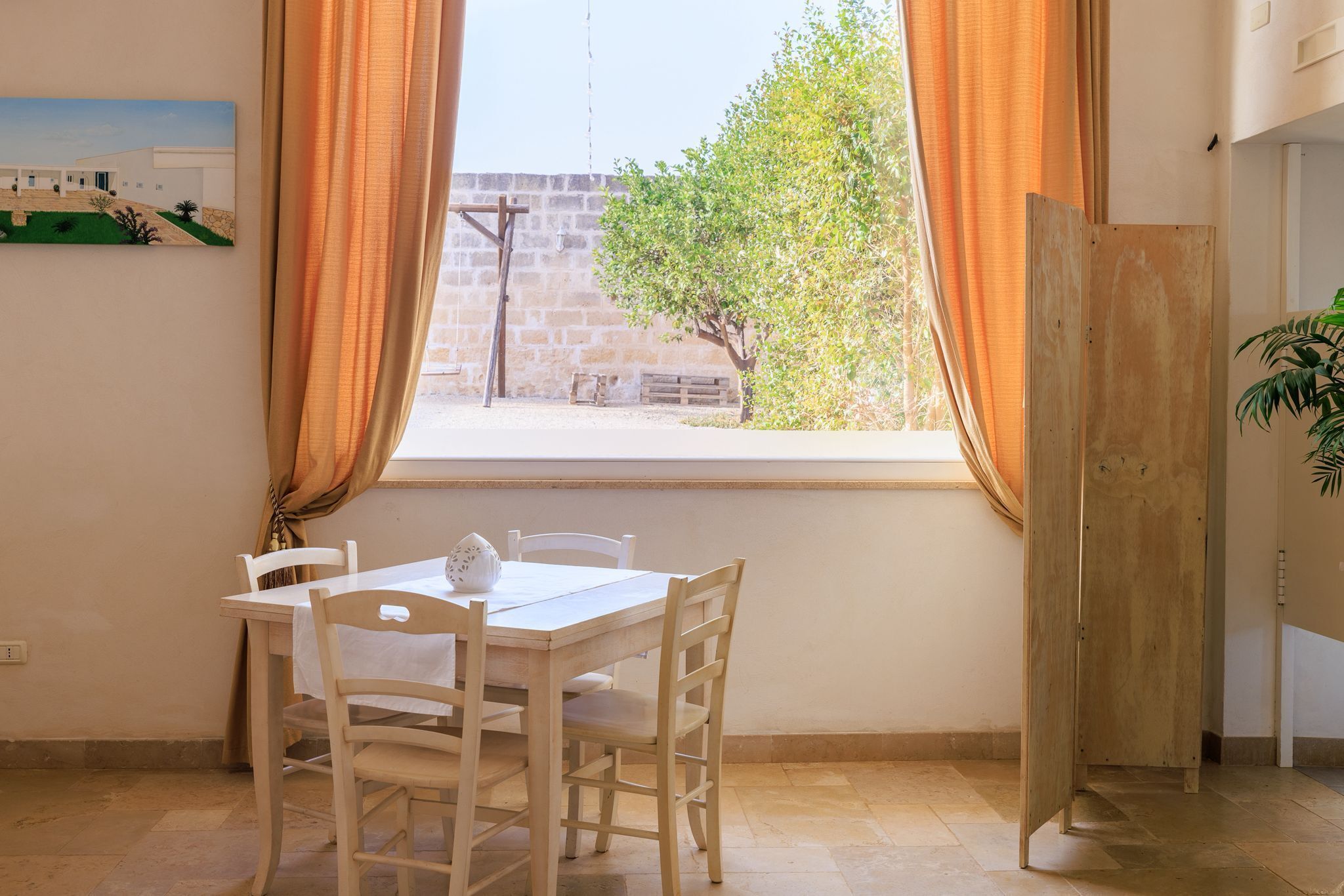 Ein Zimmer mit Esstisch, Stühlen, einem fenster mit Vorhängen, einer Holztür und einem Blumentopf.