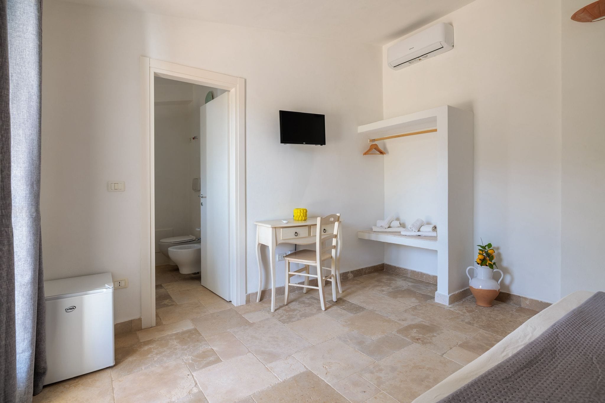 Une petite pièce propre, équipée d’un bureau, d’une chaise et d’un téléviseur fixé au mur.
