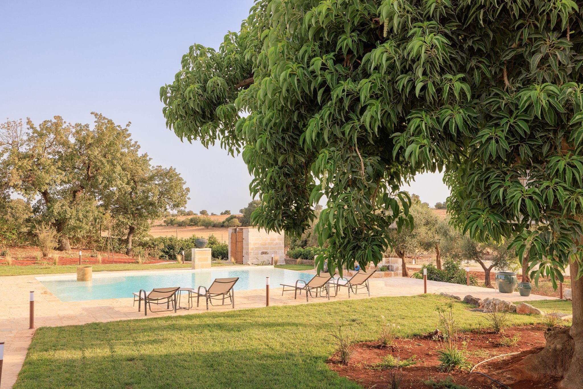 A swimming pool with lounge chairs, a stone building, and a large tree.