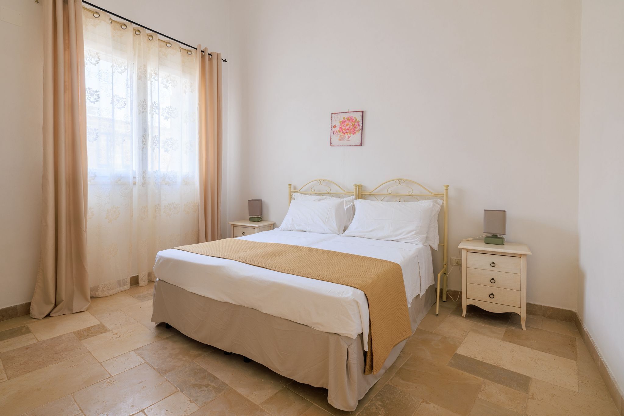 Une chambre à coucher bien rangée, avec un lit, deux tables de chevet, une petite table et un tableau accroché au mur.