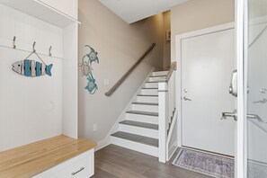 Una escalera con barandilla de madera, una puerta blanca y un adorno de pez colgado en la pared.