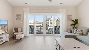 Uma sala de estar ampla com uma grande porta de vidro deslizante, ventilador de teto, televisão, sofá e mesa de centro.