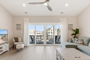 Un salón amplio con un gran ventanal corredera, un ventilador de techo, un televisor, un sofá y una mesa de centro.
