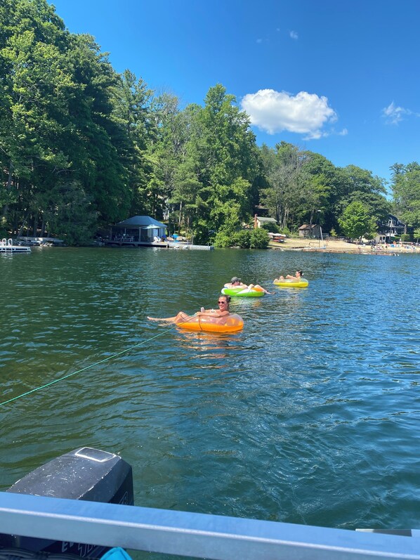 A lake with people on inflatable rafts, a dock with a covered area, and trees in the background.
