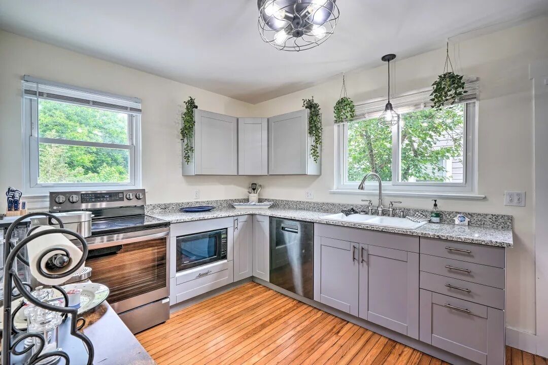 A modern kitchen with white cabinets, stainless steel appliances, and a wooden floor.