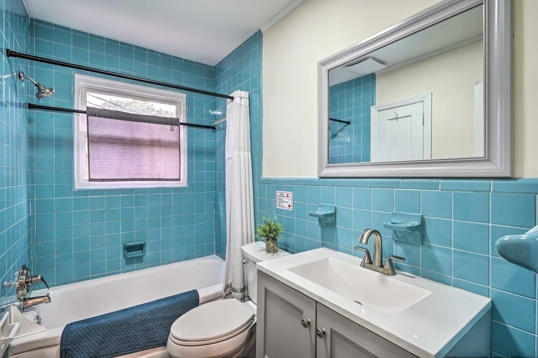 A bathroom with a bathtub, toilet, sink, and a window with a curtain.