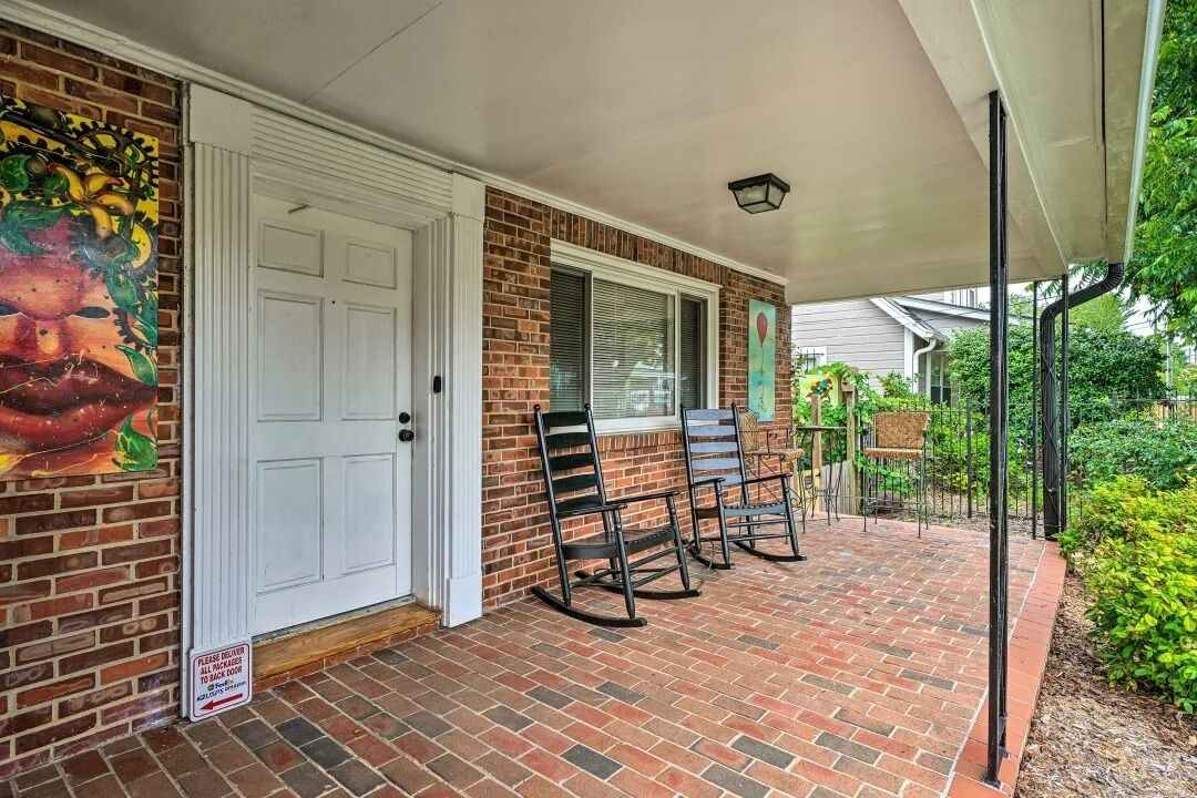 A brick porch with two rocking chairs, a white door, and a mural on the wall.
