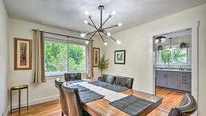 Uma área de refeições com uma mesa de madeira, cadeiras de couro, um lustre moderno e vista para a cozinha.