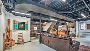 Um interior moderno com sofá de couro, dardos e escada que dá para uma cozinha.