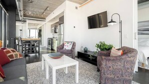 A modern living room with a white coffee table, patterned armchairs, a flat-screen TV, and a kitchen in the background.