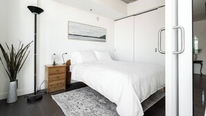 A modern bedroom with a bed, bedside table, lamp, and a painting on the wall.