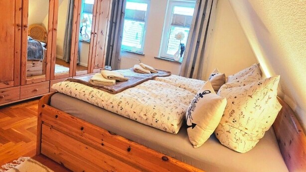 Ein Schlafzimmer mit einem Holzbett, einem Spiegel und Blick ins Freie.