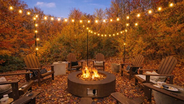 Ein Außenbereich mit Adirondack-Stühlen, einer runden Feuerstelle und Lichterketten.