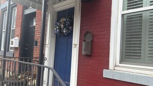 A red brick building with a blue door, a white number '4605' above the door, a metal railing in front, and a window with blinds. - Marvelous 3-bedroom townhome in vibrant upper Lawrenceville (Pittsburgh)