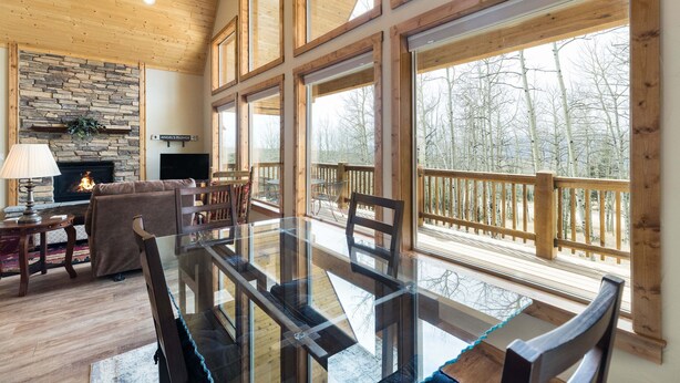 Amplia sala de estar con chimenea, ventanas grandes y una terraza con vistas a un bosque.