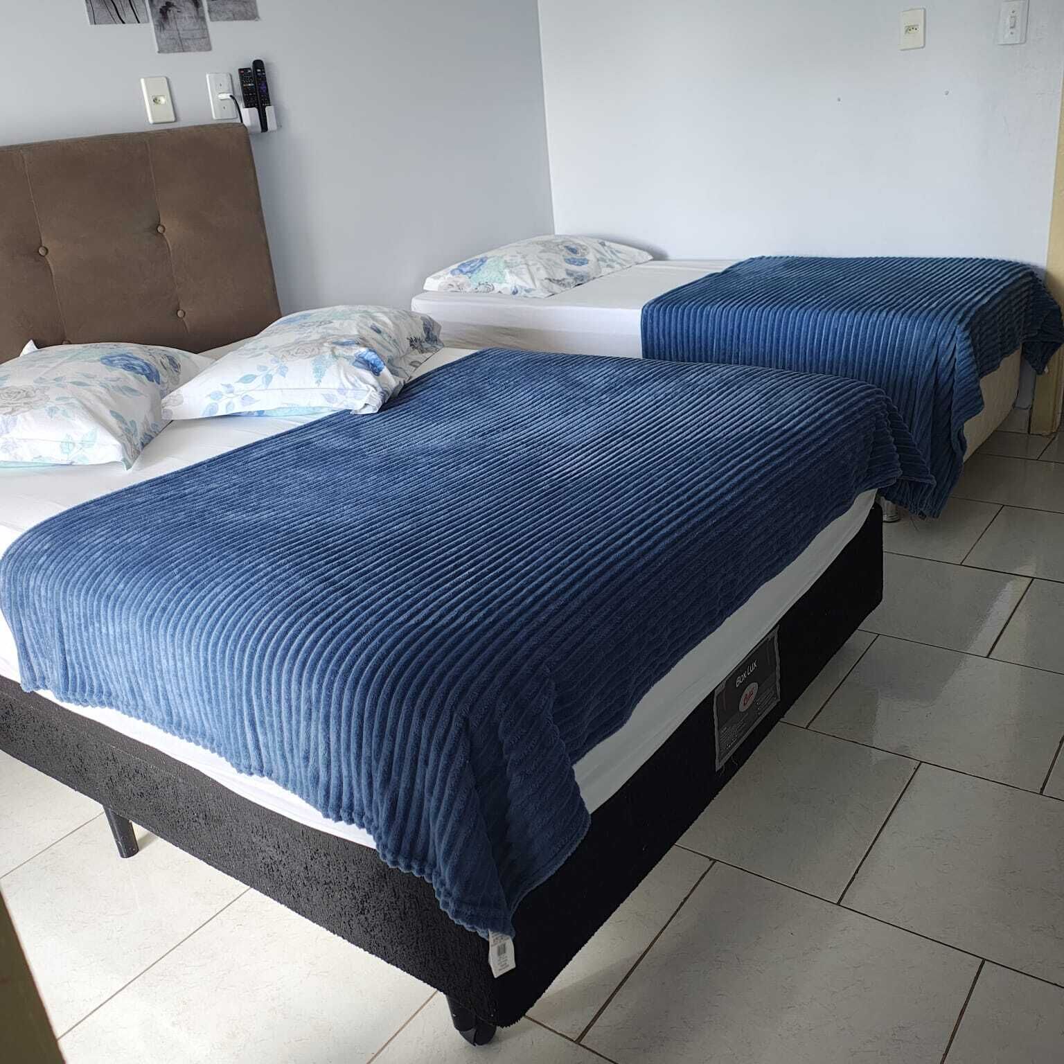 Hotellihuone, jossa on kaksi sänkyä, ruskea pääty ja laattalattia.