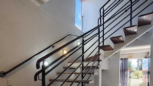 Una escalera con barandilla metálica y escalones de madera que sube a un nivel superior.