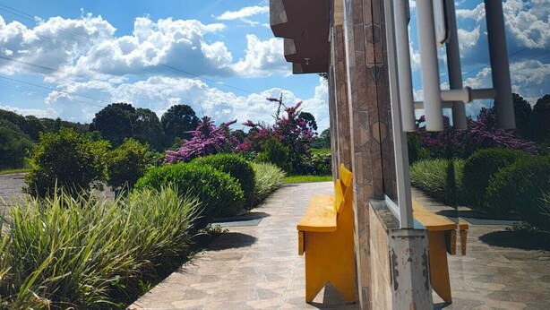 Un espacio al aire libre techado con un sendero de piedra, bancos y cielo despejado con nubes.