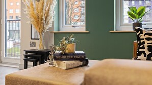 Ein Zimmer mit Fenster, Pflanze, einem Buch mit dem Titel 'The Art of Flowers' und einer Vase mit Trockenblumen.