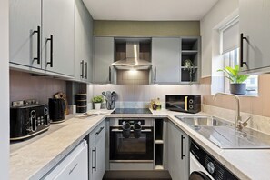A compact kitchen with built-in appliances, a stainless steel sink, and a window with a plant. - Premium Studio @ Victoria Court • Stay Angels (Broomhall)