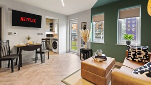 Ein modernes Wohnzimmer mit Flachbildfernseher, Essbereich, Sofa und Blick ins Freie.