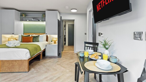 Ein modernes Hotelzimmer mit Bett, Nachttisch, Frühstückstisch und einem Fernseher, der das Netflix-Logo zeigt.