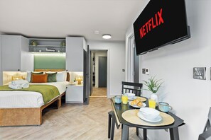 A modern hotel room with a bed, bedside table, breakfast table, and a TV displaying the Netflix logo. - Premium Studio @ Victoria Court • Stay Angels (Broomhall)