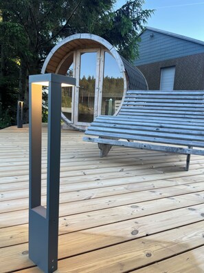 A wooden deck with a bench and a circular wooden structure with glass doors.