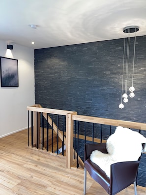 A modern interior with a wooden staircase, a dark brick wall, and a hanging light fixture.